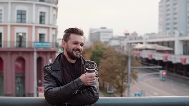 A stylish handsome man with a beard and trendy haircut smiling cheerfully, holding takeaway coffee or tea. Slow mo — Stock Video