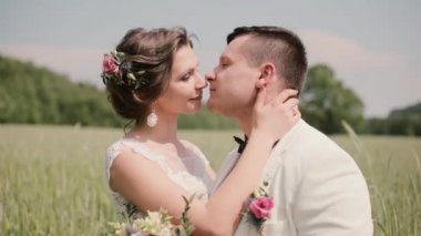 Mutlu çift aşık bir düğün gününde bir buğday alanındaki samimi an ayakta paylaşmak. Gelin ve damat şefkatle öpüşme.