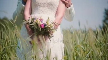 Güzel düğün buket buğday alanında onun damat ile ayakta bir gelinin elinde close-up. Rüzgarda sallanan koniler