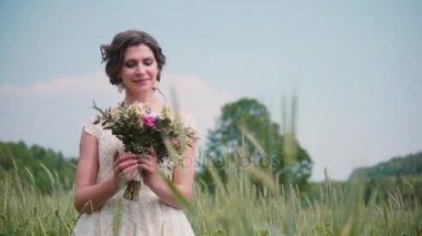 Bir buğday alanında ayakta onu düğün buket bakarak çok güzel bir genç gelin. Ona oldukça dantelli gelinlik.