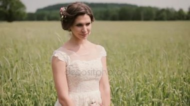 Beyaz dantelli gelinlik içinde güzel bir gelin görünümünü, o bir buğday alanında ayakta onu elinde bir buket tutar.