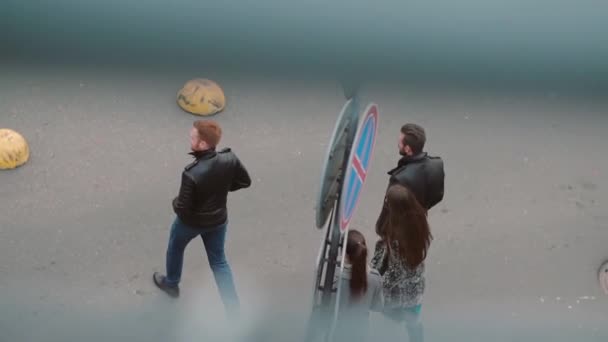 Vista desde la parte superior de la calle donde caminan cuatro personas con estilo. Dos chicas y dos hombres cruzan la calle. Lento mo, steadicam tiro — Vídeo de stock