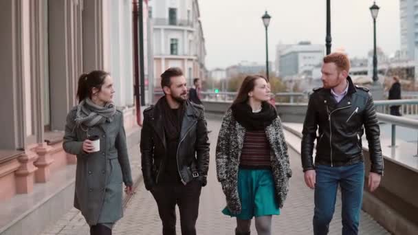 Young people walk in the city. Two pretty girls and two handsome young men talk on the go. Slow mo, steadicam shot — Stock Video