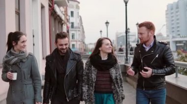 Dört şık genç insanların şehirde, adam Kızıl saçlı görüşmeleri ile yürümek, diğerleri dinle ve gülümse. Yavaş mo, steadicam vurdu
