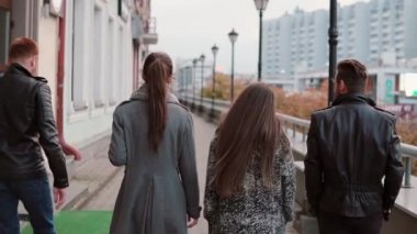 İki trendy kız ve iki şık erkek şehirde yürümek. Arka plan binalara. Yavaş mo, steadicam shot, arkadan görünüm