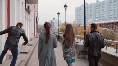 İki trendy kız ve iki şık erkek neşeyle şehirde yürüyüş, atlama ve eğlenin. Yavaş mo, steadicam shot, arkadan görünüm