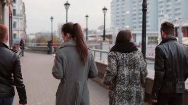 İki trendy kız ve iki şık erkek neşeyle şehir ve konuşma yürümek. Yavaş mo, steadicam shot, arkadan görünüm