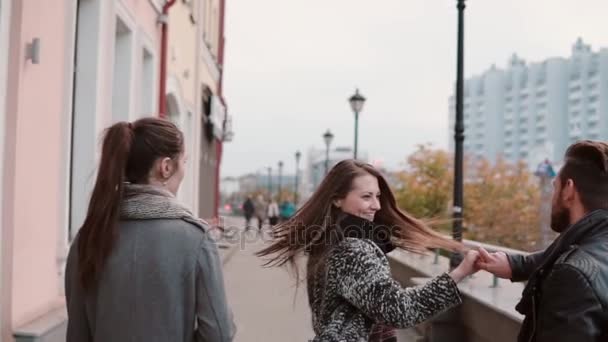 Junge Leute spazieren fröhlich durch die Stadt, zwei von ihnen tanzen ein bisschen, lächeln und haben Spaß. slow mo, steadicam shot, rückseite — Stockvideo