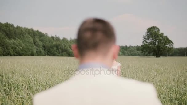 Rückansicht eines Bräutigams, der am Hochzeitstag seiner schönen Braut in einem Weizenfeld entgegenkommt und sie küsst. — Stockvideo