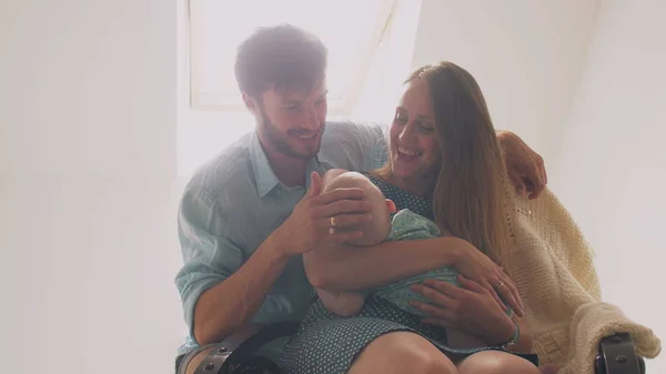 Прекрасная счастливая мать семьи убаюкивает своего ребенка в кресле-качалке, отец хлопает по голове своего сына и целует жену. 4k — стоковое фото