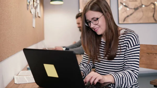 Young attractive girl working with laptop in a modern startup office — Stock Photo, Image