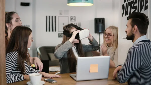 Chica morena intenta aplicación para gafas de realidad virtual casco VR sus amigos y colegas que la apoyan en la oficina moderna — Foto de Stock