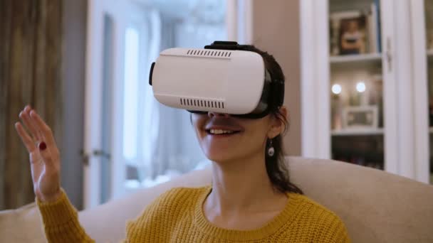 Красива молода жінка сидить на дивані у вітальні і використовує гарнітуру VR. 4-кілометровий — стокове відео