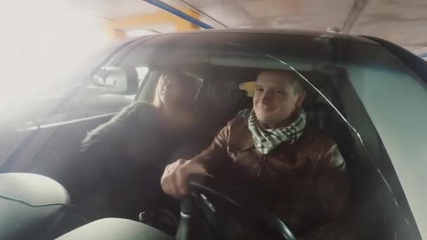 Un uomo e una donna sorridenti seduti in macchina, guardano attraverso il finestrino di un'auto. Fotocamera attaccata al paraurti anteriore . — Video Stock