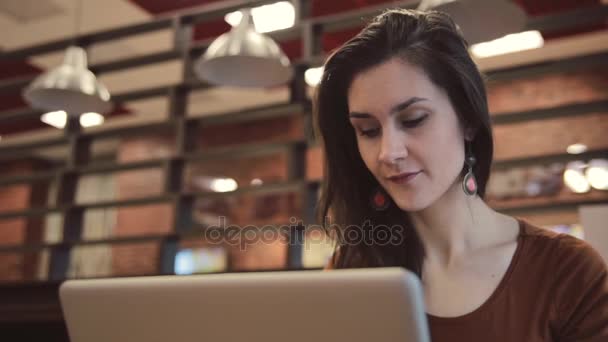 Chica morena joven trabajando en el ordenador portátil en la cafetería . — Vídeo de stock