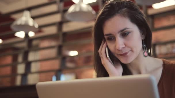 年轻的黑发女孩笔记本电脑上工作，和谈在咖啡馆电话. — 图库视频影像