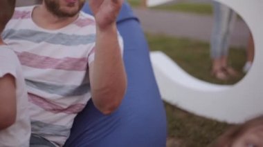 Mutlu aile baba oğul ve kızının çanta sandalyeler Park'ta oturuyor. Erkek ve kız pizza, saç stoking baba yemek
