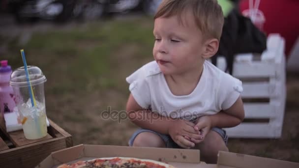 Jovem mulher bonita e menino ter um descanso no parque no dia de verão. Menino comendo pizza e depois aponta para sua mãe . — Vídeo de Stock