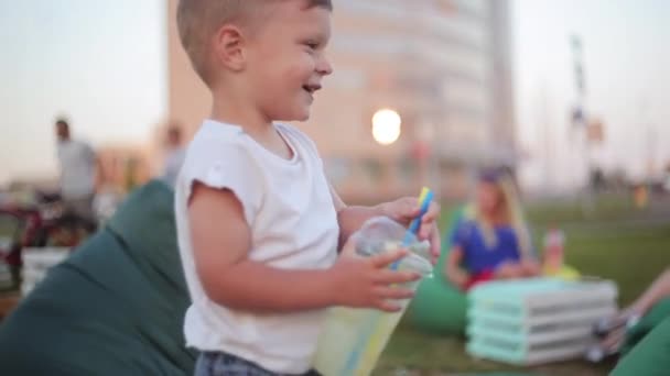 Pretty little boy having fun at the park in summer day, holding a glass with straws and laughing. — Stock Video