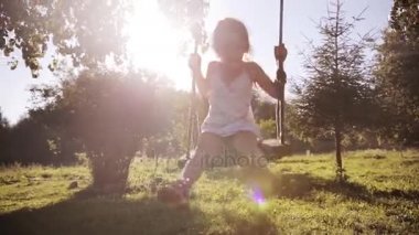 Sevimli küçük güzel kız bir ağacı salıncak ve gülümseme salıncak üzerinde parkta sunset bulvarında eğleniyor