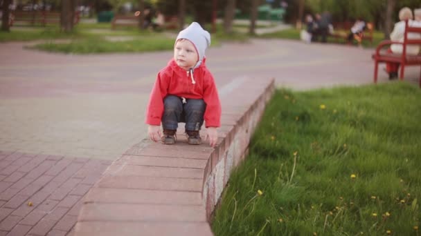 Cute baby boy playing outdoor squatting at the park near to the green grass and looking around. — Stock Video