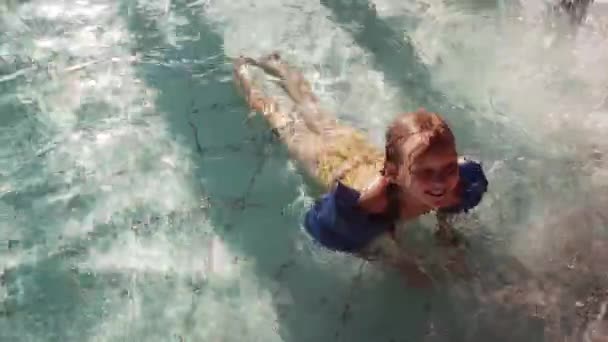 Szép kislány az aquapark szórakozás. Aranyos lány felfújható karszalagok feküdt a medence vízbe. Szemközti nézet — Stock videók