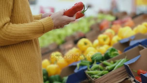 Nahaufnahme der Hand einer Frau, die im Supermarkt eine rote Paprika auswählt und diese in der Hand hält. Vitrine mit Gemüse. 4k — Stockvideo