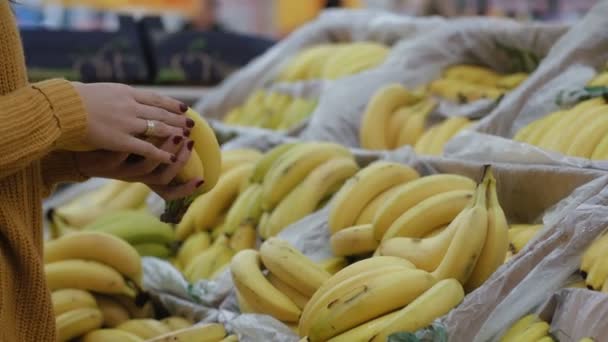 Крупним планом, молода жінка, вибираючи банани в супермаркеті, тримає деякі. Вітрина з фруктами. 4-кілометровий — стокове відео