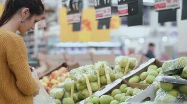 Bir meyve ve sonra yerine pakete tutan genç kadın bir yeşil elma süpermarkette, seçme. 4k