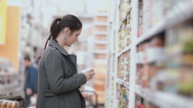 Önünde duran genç güzel kadın ile bakkal raflarında, olabilir bir tane tuttuğunu ve süpermarkette seçmek deneyin. 4k