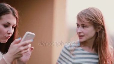 İki güzel womanare smartphone kullanarak ve konuşma. Arkadaşlar telefon yaz aylarında açık fotoğrafları izlerken.