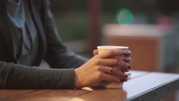 Närbild av kvinna s hand som håller en kopp kaffe, rök från te koppen. Suddig lampor, urban street — Stockvideo