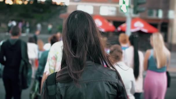 Mujer morena joven cruzando la calle en la ciudad, pelo revoloteando en el viento. cámara lenta, disparo steadicam, vista trasera . — Vídeo de stock