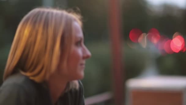 Attraktive lächelnde junge Frau im Stadtcafé. Nahaufnahme, verschwommenes Licht, Stadtstraße, Seitenansicht — Stockvideo