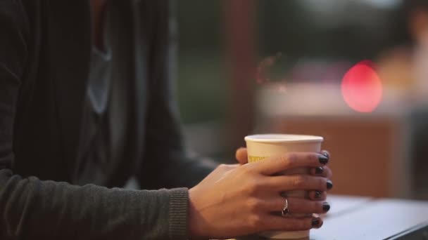 Close-up van vrouw s hand hebt van een kopje koffie, camera beweegt omhoog aan het gezicht van de meisjes. Wazig lights achtergrond. — Stockvideo