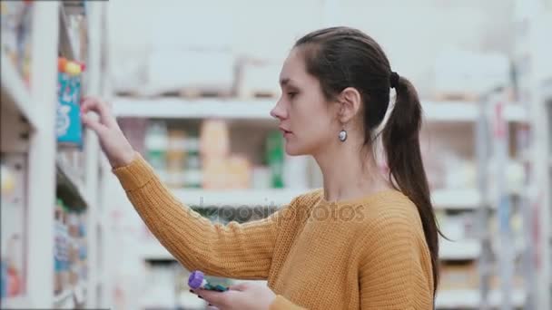 Mooie jonge vrouw kiest babyvoeding in de supermarkt in de buurt van de voedsel-plank. 4k — Stockvideo