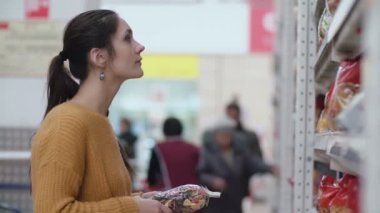 Önünde duran genç güzel kadın bir ve deneyin bir şey süpermarkette seçmek holding ile makarna, temizleyelim. 4k