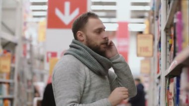 Genç telefon tutarak ve çağrı süpermarket raflarında, önünde duran adam. Madde ve tavsiye istiyorum alır. 4k