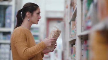 Önünde duran genç güzel kadın bir ve deneyin bir şey süpermarkette seçmek holding ile kabuğu çıkarılmış tane, temizleyelim. 4k