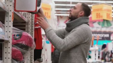 Genç adam ürünler raflarda süpermarkette, seçme istiyor güle güle Bebek Oto Koltuğu için kalite kontrol. 4k