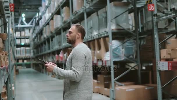 Jeune homme utilisant une tablette numérique en entrepôt, vérifier la liste des marchandises au supermarché. Touchez les boîtes en carton. 4K — Video
