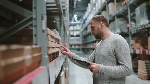 Jonge man met behulp van digitale tablet in magazijn, controleren van de lijst van goederen te kopen bij de supermarkt en op zoek naar artikelen. 4k — Stockvideo