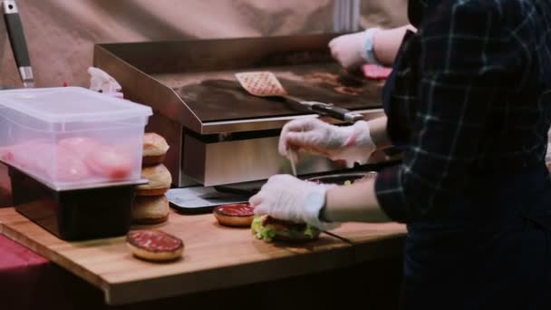 Un chef con guantes blancos hace hamburguesas. Hombre poniendo pero en la parte superior de las hamburguesas y pinchos perfora cada hamburguesa Vista posterior — Vídeo de stock