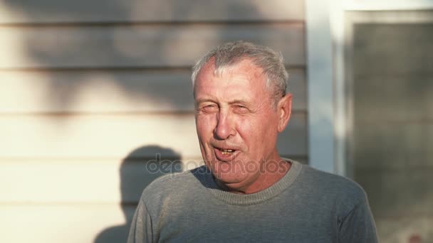 Close-up van lachende oude man gezicht staande voor camera, glimlachen, lachen, praten buiten in zonlicht. 4k — Stockvideo