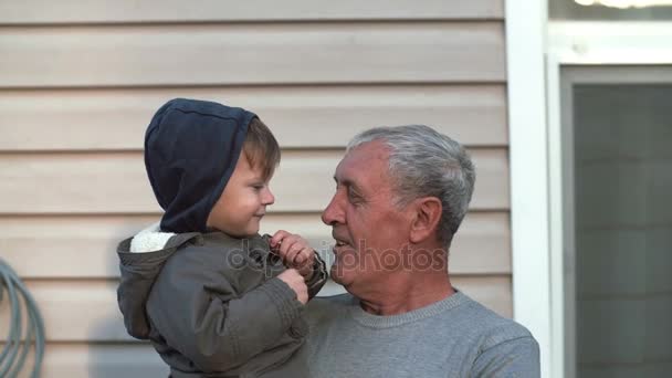 Старик держит маленького мальчика под рукой. Дедушка развлекается с внуком, трогай ухо. Мальчик показывает пальцем к носу. 4K — стоковое видео
