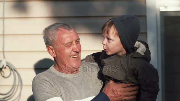 Старик держит маленького милого мальчика на руках, посмотри на него. Внук указывает на что-то пальцем, дедушка смотрит. 4K — стоковое видео