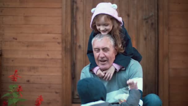 Little girl standing behind old man. Granddaughter hugs grandfather, grandson running to they. Boy sits on man knees. 4K — Stock Video