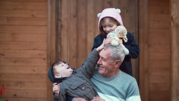 Niño sentado en las rodillas del abuelo, chica de pie detrás y abrazo. Hermano y hermana jugando con ovejas de juguete, riendo. 4K — Vídeos de Stock