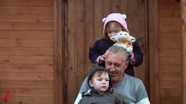 Jongen op grootvader knieën zittend. Meisje die achter, spelen met speelgoed schapen. Broer en zus plezier buiten. 4k — Stockvideo