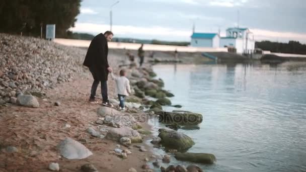 Vader en zoon op strand hand in hand en wandelen langs de kust bij zonsondergang. Meisje loopt tot man. Vader knuffels dochter. — Stockvideo